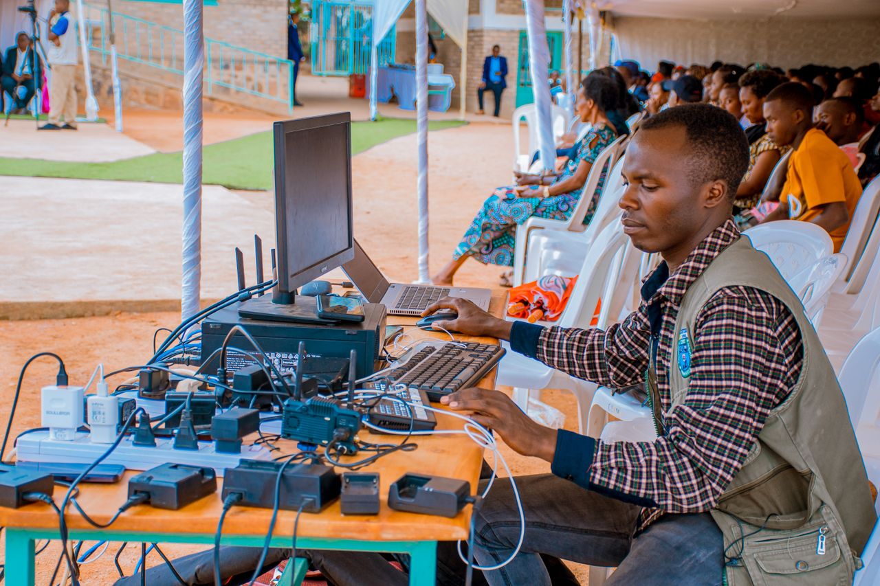 gallery-4 Technician managing electrical and computer setup at an outdoor event with attentive audience.